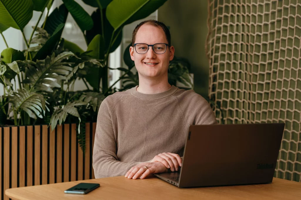 Een consultant legt uit hoe certificering werkt. Consultant zit aan tafel, achter een laptop.